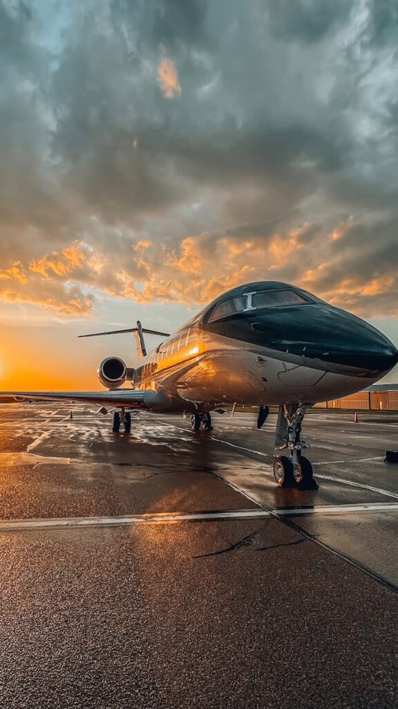 A sleek private jet parked on a wet tarmac during a colorful sunset at an airport.