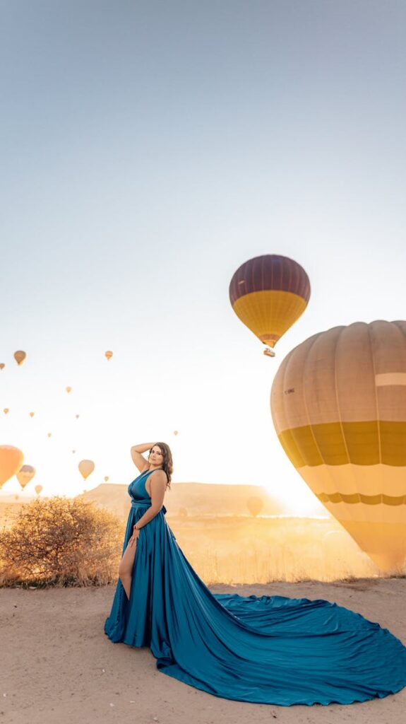 Elegant woman in a blue dress posing with colorful hot air balloons in the background.