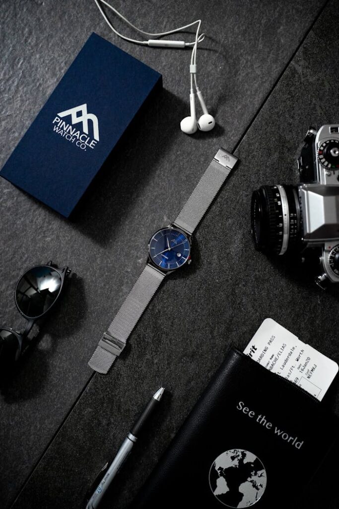 Stylish flat lay of watch, camera, passport, and travel items on dark surface.
